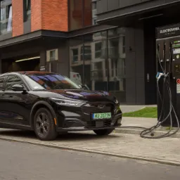 Czarny samochód elektryczny Ford Mustang Mach-E ładowany przy stacji Elektrownia Powiśle, widoczna tablica rejestracyjna WU 2071M.