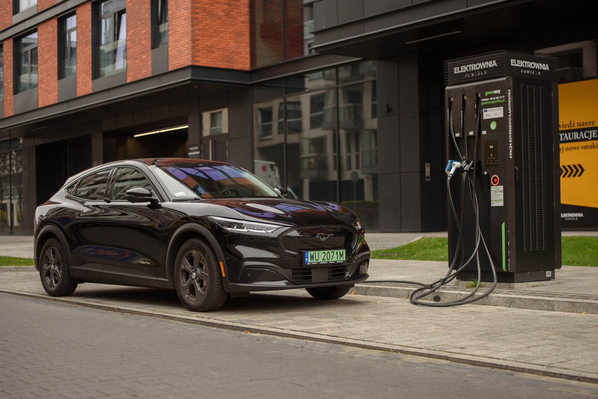 Czarny samochód elektryczny Ford Mustang Mach-E ładowany przy stacji Elektrownia Powiśle, widoczna tablica rejestracyjna WU 2071M.