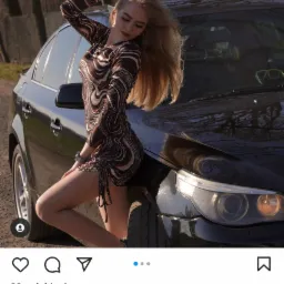 Młoda kobieta w wzorzystej sukience pozuje oparta o czarny samochód na zewnątrz.