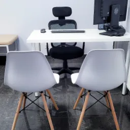 Gabinet lekarski z dwoma krzesłami dla pacjentów, biurkiem z komputerem i ergonomicznym krzesłem obrotowym.