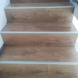 Schody wyłożone panelami imitującymi drewno, zabezpieczone srebrnymi listwami na krawędziach stopni, widok z góry.