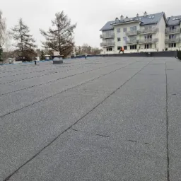 Wykończony płaski dach pokryty papą termozgrzewalną na budynku wielorodzinnym. Widoczna osoba w odblaskowej kamizelce na krawędzi dachu.