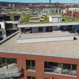 Dachowe Love - Nowoczesny budynek z płaskim dachem pokrytym drobnym żwirem i zielenią. Widok z góry na architekturę miejską w słoneczny dzień.