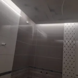 Wykończona łazienka z szarymi i białymi płytkami, dekoracyjnym pasem płytek w romby i oświetleniem LED podsufitowym.