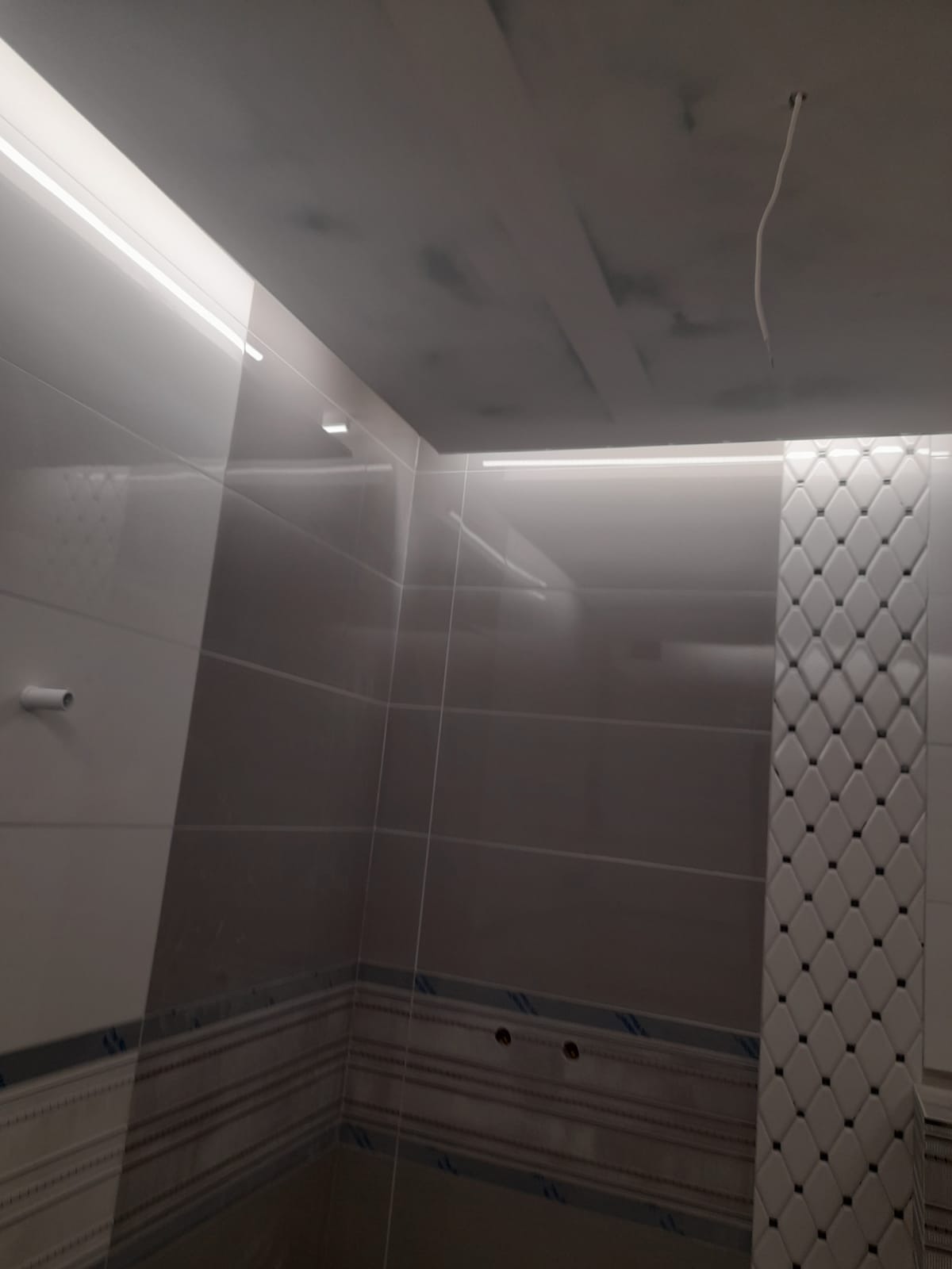 Wykończona łazienka z szarymi i białymi płytkami, dekoracyjnym pasem płytek w romby i oświetleniem LED podsufitowym.