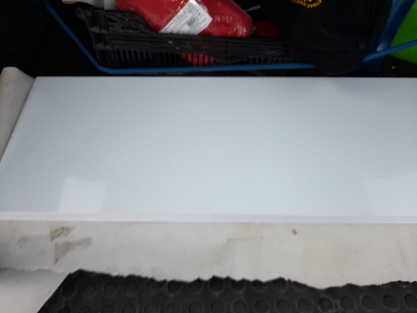 Biała płyta gipsowo-kartonowa w trakcie transportu, widoczne uszkodzenia na krawędziach i fragment podłogi z gumową wyściółką.