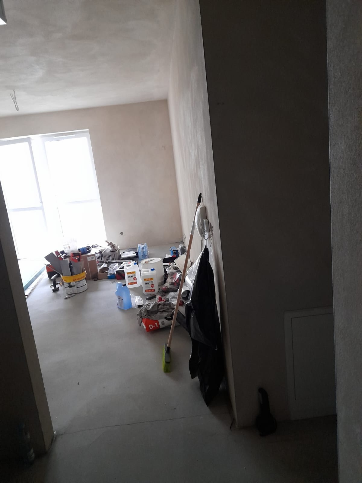 Wnętrze pokoju w trakcie prac wykończeniowych: widoczne wiaderka z farbą, pojemniki z zaprawą, narzędzia malarskie i szpachlarskie, ściany przygotowane do malowania lub szpachlowania, podłoga...