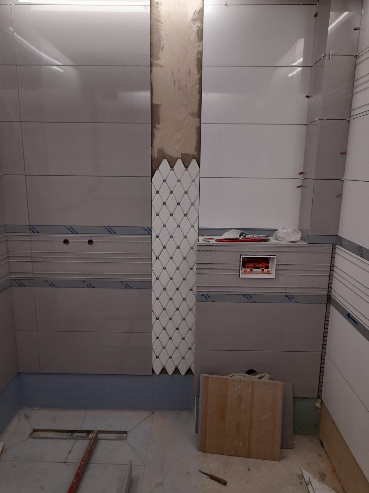 Montaż dekoracyjnej mozaiki romboidalnej na ścianie w łazience, widoczne narzędzia i płytki w trakcie układania.