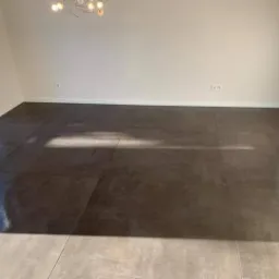 Nowoczesne, brązowo-szare płytki podłogowe w pustym, jasnym pokoju z dużym oknem i designerską lampą sufitową.