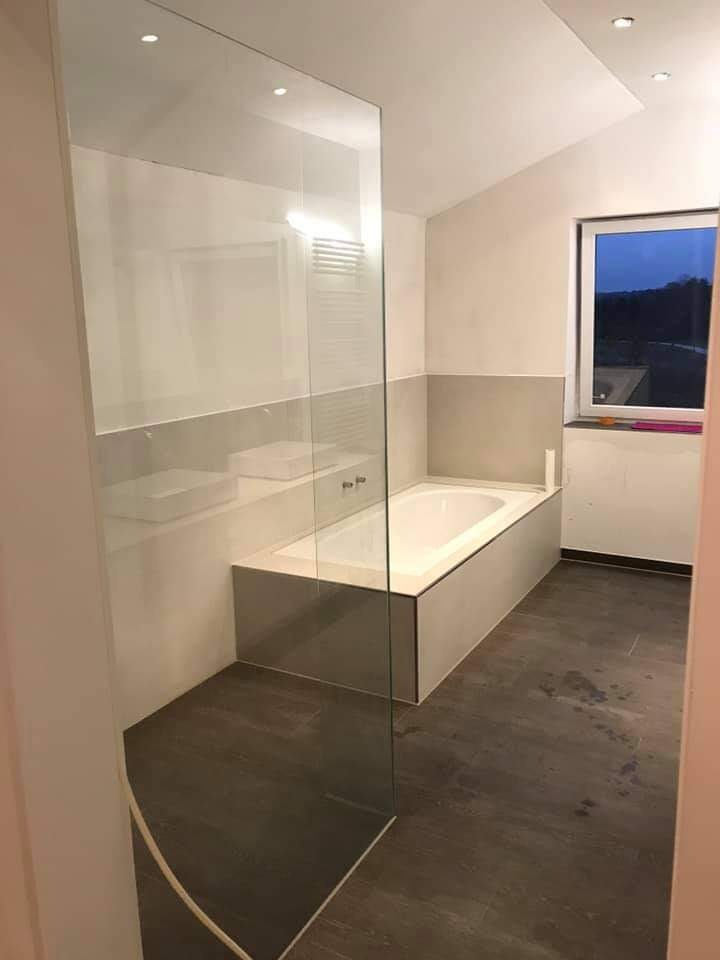 Nowoczesna łazienka z kabiną prysznicową typu walk-in, białą wanną w zabudowie i ciemną podłogą imitującą drewno, oświetlona punktowymi lampami sufitowymi.