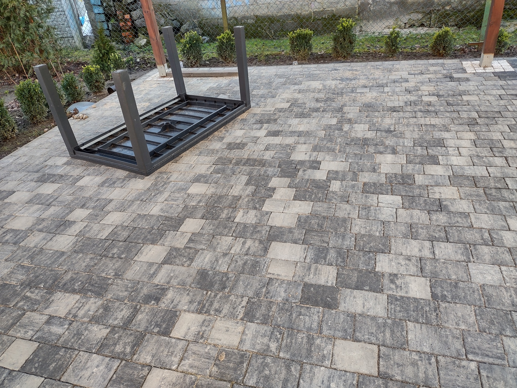 Ułożona kostka brukowa w odcieniach szarości z elementem konstrukcyjnym stołu w tle, widok z góry.