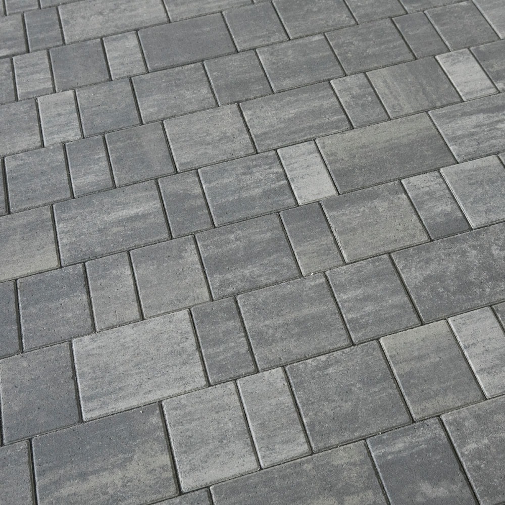 Szara kostka brukowa ułożona w regularny wzór, widok z góry pod kątem, z delikatną teksturą i widocznymi fugami.