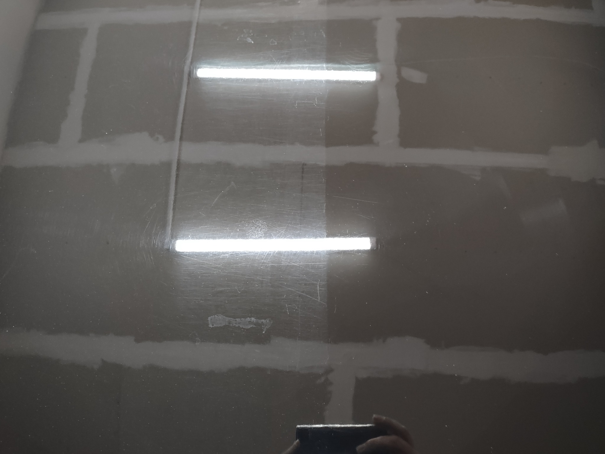 Świeżo położona gładź szpachlowa na ścianie, widoczne łączenia płyt gipsowo-kartonowych oraz odbicie lampy sufitowej.