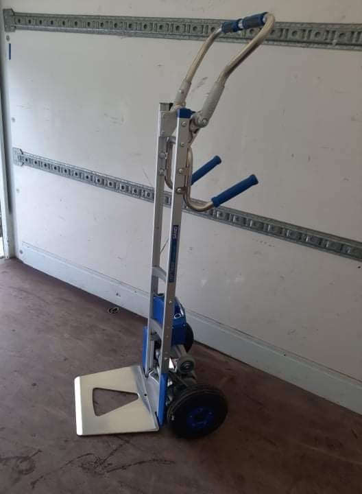 Wózek schodowy elektryczny z niebieskimi uchwytami wewnątrz furgonetki z systemem mocowania ładunku.
