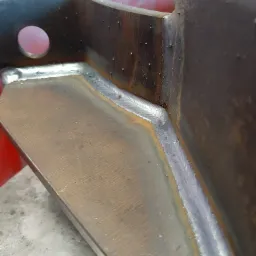 Szczegółowe zbliżenie na spawany narożnik konstrukcji stalowej z widocznymi śladami spawania i otworem w górnej części.