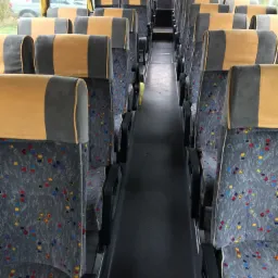 Wnętrze autobusu z rzędami szarych siedzeń z kolorowymi wzorami i żółto-szarymi zagłówkami, widok wzdłuż korytarza.