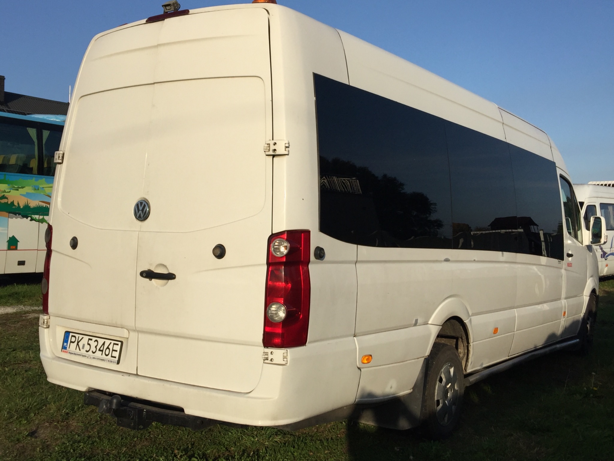 Tył białego busa z przyciemnianymi szybami i tablicą rejestracyjną PK 5346E, hak holowniczy, na trawie.