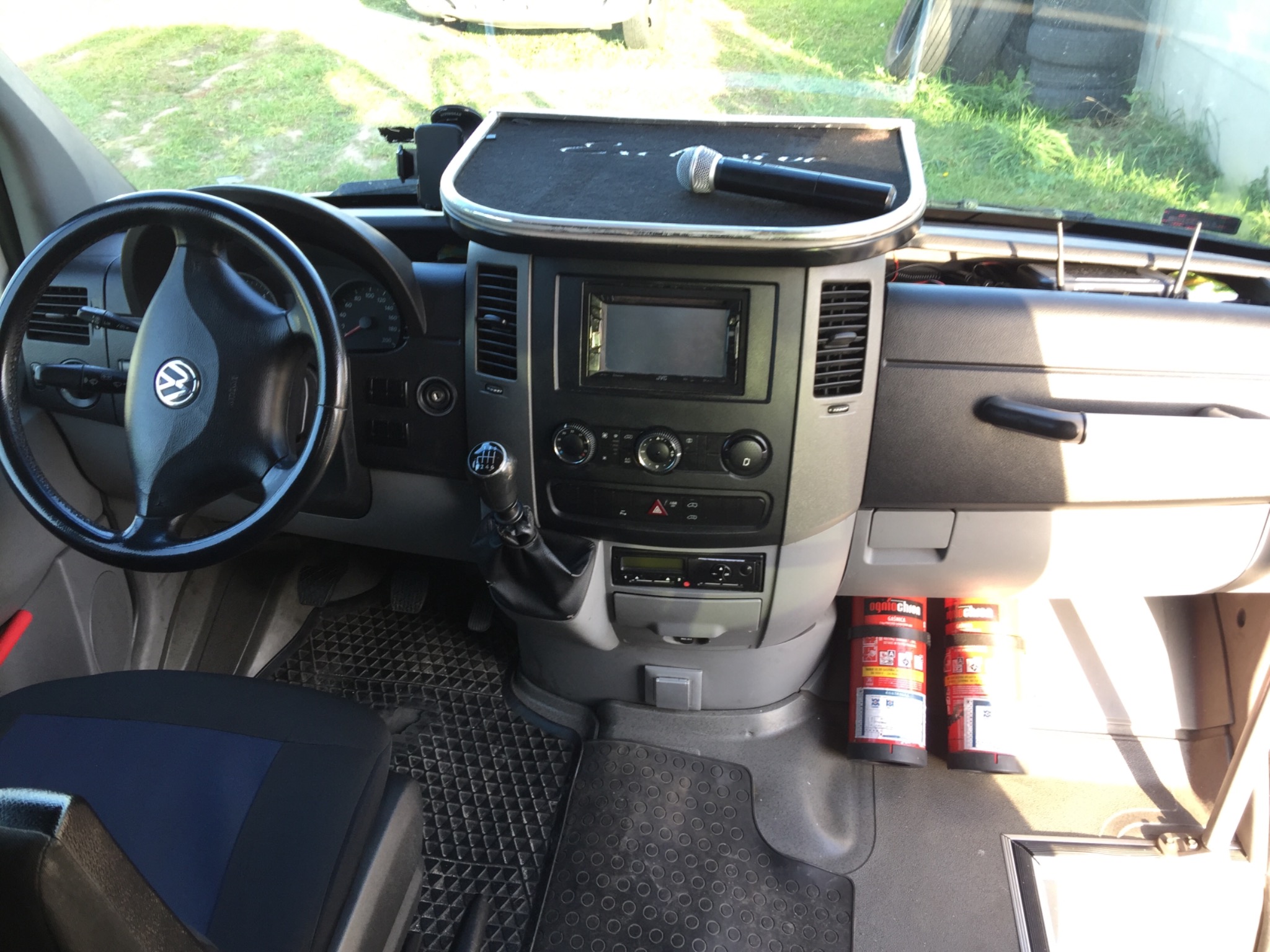 Wnętrze busa z mikrofonem na desce rozdzielczej i gaśnicami pod schowkiem, widok z perspektywy kierowcy.