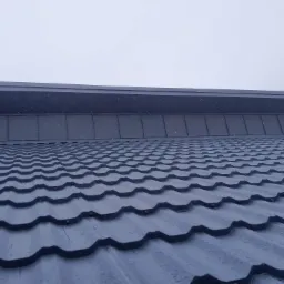 Nowe, metalowe pokrycie dachowe w Leśnicy, widoczne z bliska, z kroplami wody na powierzchni w pochmurny dzień.