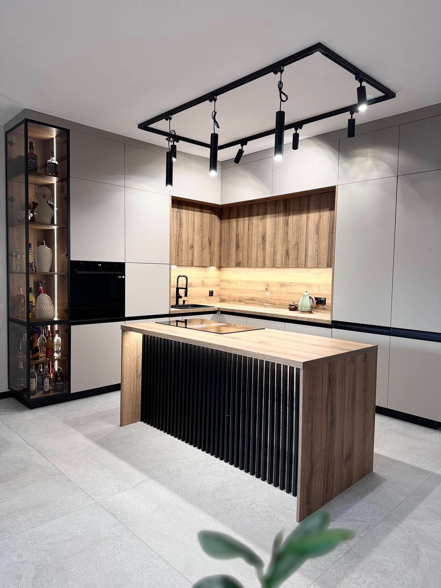 Nowoczesna kuchnia z wyspą wykończoną pionowymi, czarnymi listwami, szklana witryna z oświetleniem LED eksponująca alkohole i dekoracje, oraz minimalistyczne oświetlenie sufitowe.