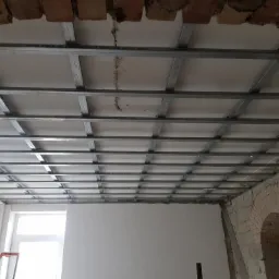 Stelaż z profili stalowych pod montaż płyt gipsowo-kartonowych na suficie, widoczne fragmenty surowego muru i cegieł