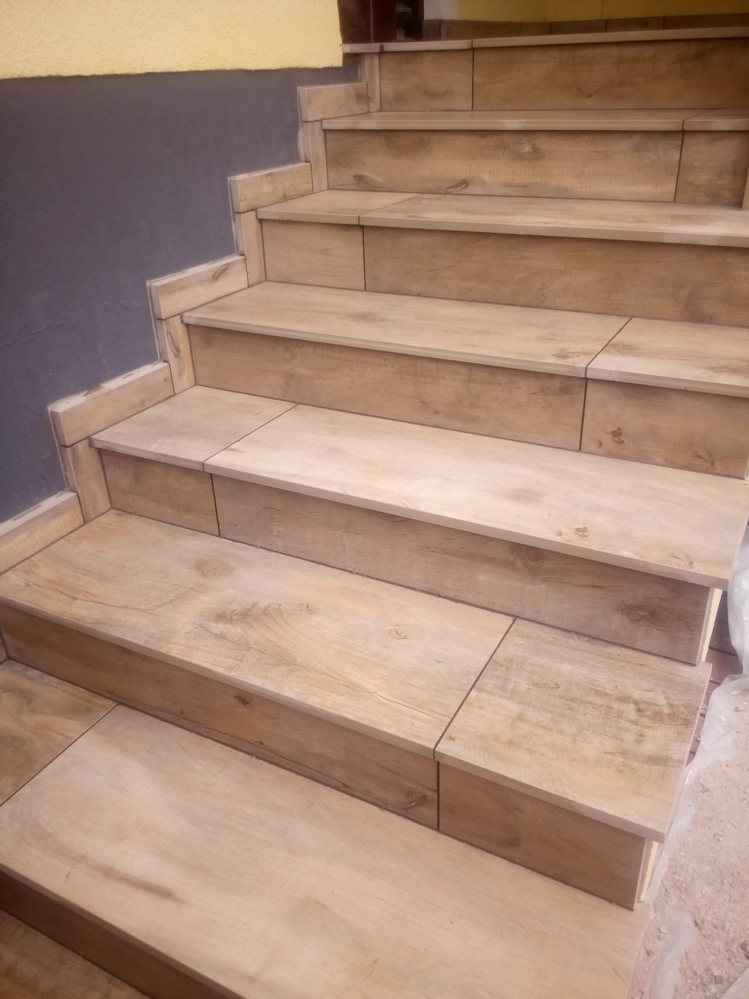 Wyłożone płytkami imitującymi drewno schody wewnętrzne z szarą ścianą w tle, widok z dołu.