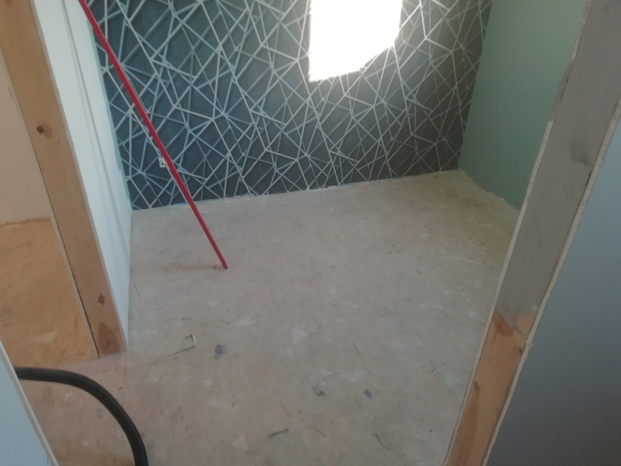 Pokój w trakcie remontu: podłoga przygotowana pod układanie parkietu, ściana z geometryczną tapetą i fragment pomalowanej na jednolity kolor ściany, widoczne elementy konstrukcji drzwi i rura...