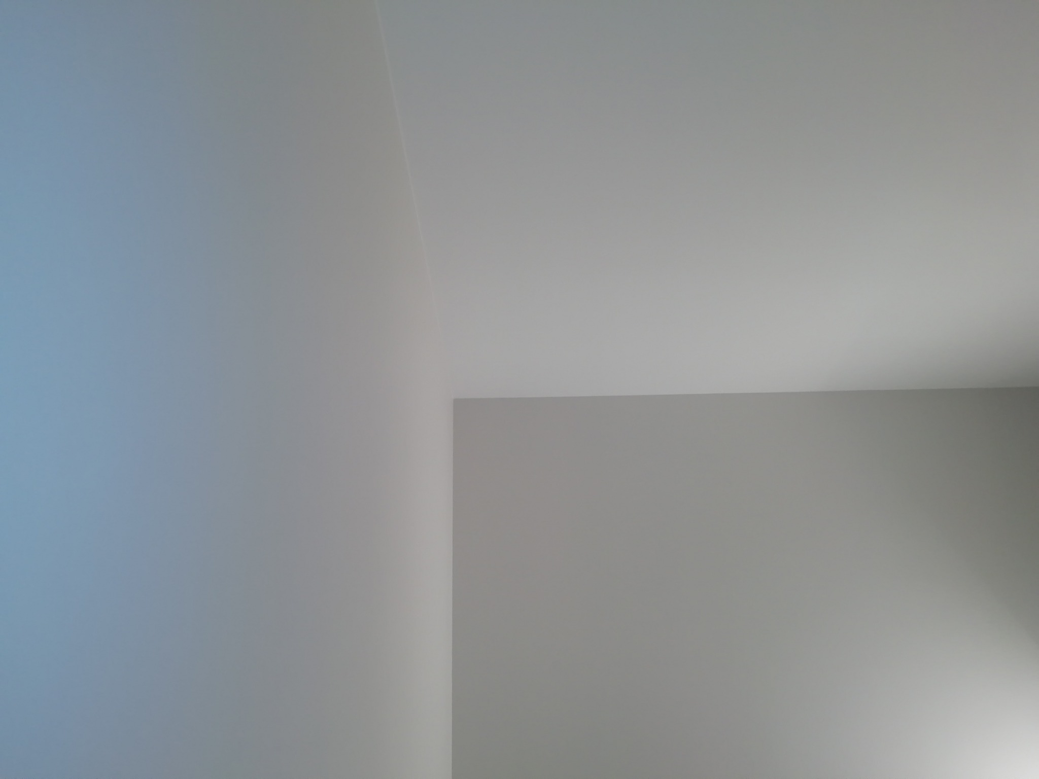 Fragment pomalowanego na szaro i biało wnętrza, widoczne połączenie ściany z sufitem pod kątem, oświetlone z prawej strony.