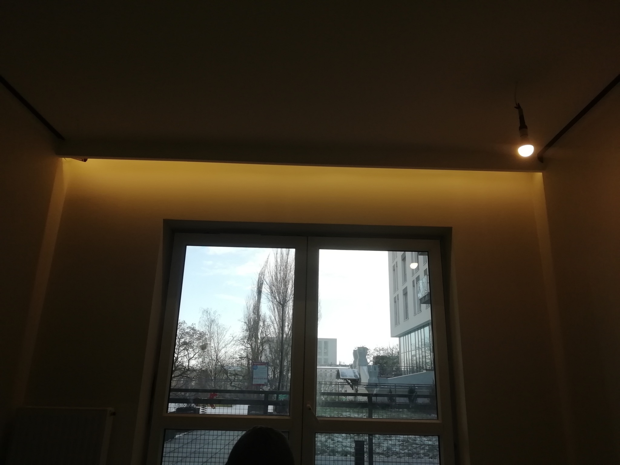 Pokój z oświetleniem LED podsufitowym i widokiem na nowoczesny budynek przez okno w pochmurny dzień.