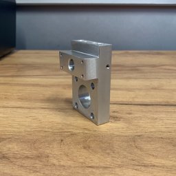 CUSTOM-MET Maciej Franc - Precyzyjnie obrobiony, srebrny element metalowy z otworami o różnych średnicach, leżący na drewnianej powierzchni.