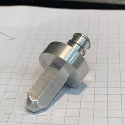 CUSTOM-MET Maciej Franc - Metalowy element obrobiony na tokarce, leżący na kartce w kratkę. Widoczne ślady obróbki skrawaniem.