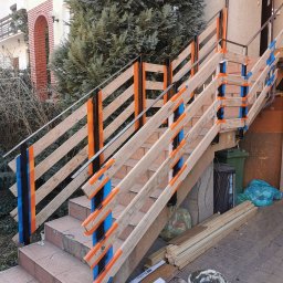 Krystian koseski - Zewnętrzne schody z drewnianą balustradą w trakcie renowacji, zabezpieczone taśmą malarską, widoczny kubeł z masą szpachlową, przygotowane deski i worki na śmieci