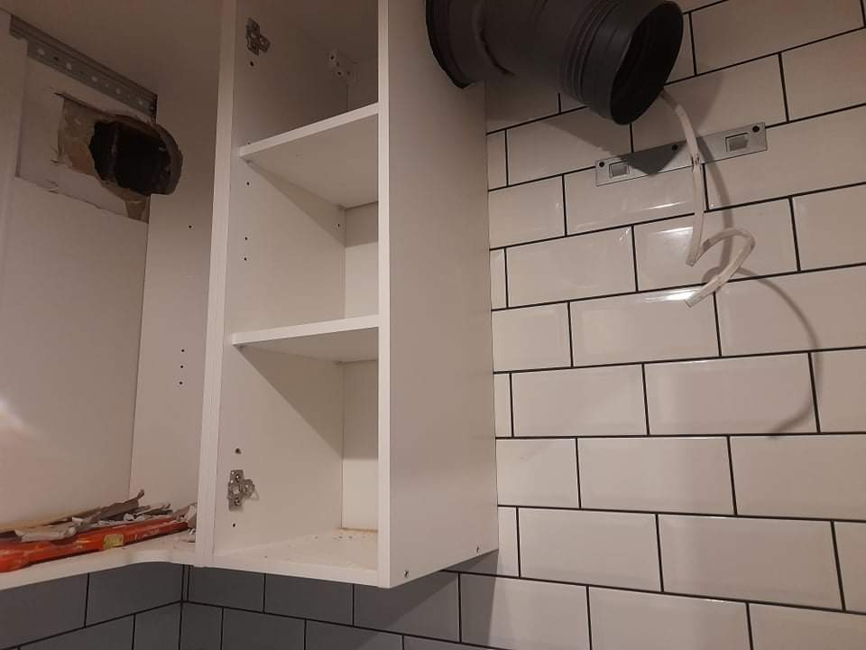 Bielsk Podlaski: Montaż szafki kuchennej w trakcie remontu, widoczny fragment instalacji wentylacyjnej oraz świeżo położone białe płytki z ciemną fugą.