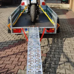 Motocykl zabezpieczony pasami transportowymi na przyczepce samochodowej z najazdem, widok z tyłu, tablica rejestracyjna TIR IV11.