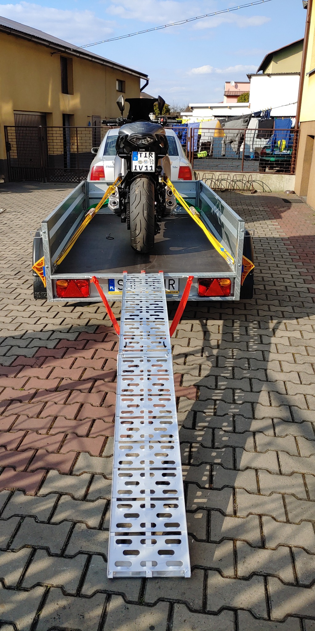 Motocykl zabezpieczony pasami transportowymi na przyczepce samochodowej z najazdem, widok z tyłu, tablica rejestracyjna TIR IV11.