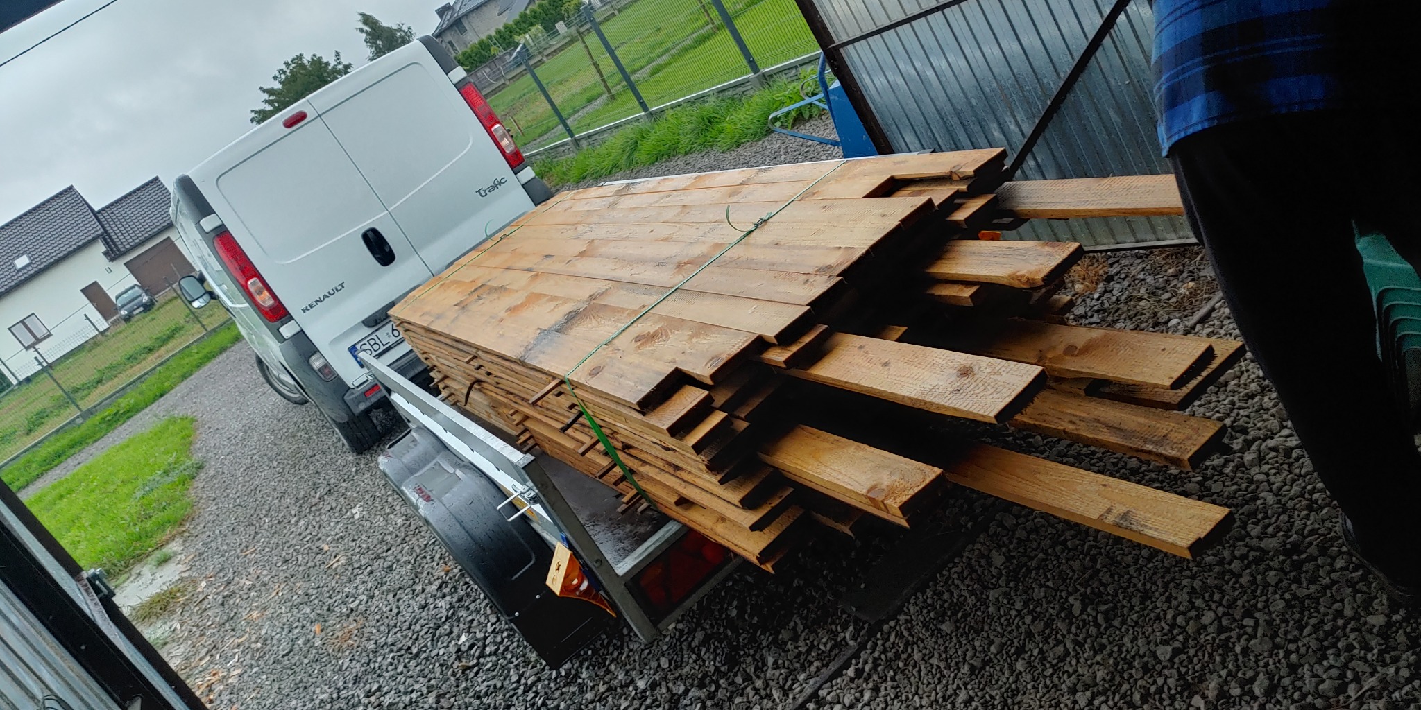 Transport desek busem w Jedlinie, deski ułożone na przyczepce za białym Renault Trafic, widoczne numery rejestracyjne.