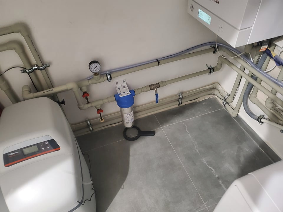 Zestaw instalacji wodnej z filtrem, manometrem i zmiękczaczem wody Viessmann, rury prowadzone wzdłuż ściany, szare płytki podłogowe.