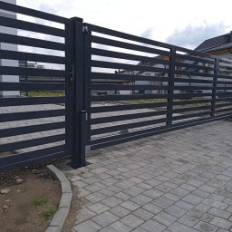 P.P.H.U. MM MAŁGORZATA KITA - Nowoczesna, przesuwna brama wjazdowa z poziomymi, szarymi panelami metalowymi i widoczną kostką brukową na podjeździe, na tle domu.