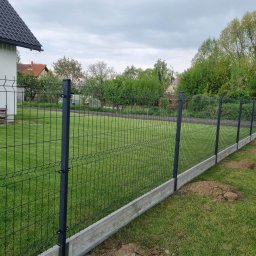 P.P.H.U. MM MAŁGORZATA KITA - Ciemna siatka panelowa zamontowana na betonowej podmurówce, widok na trawnik i dom w tle. Świeżo usypana ziemia przy ogrodzeniu.