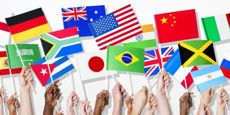 Różnorodne ręce trzymające flagi różnych krajów na białym tle, symbolizujące globalną współpracę i marketing międzynarodowy.