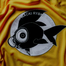 Żółta koszulka sportowa z nadrukowanym logo klubu pływackiego 'Klub Pływacki Rybka Goldi Akademia Niemowlaka' w kształcie czarnej ryby.