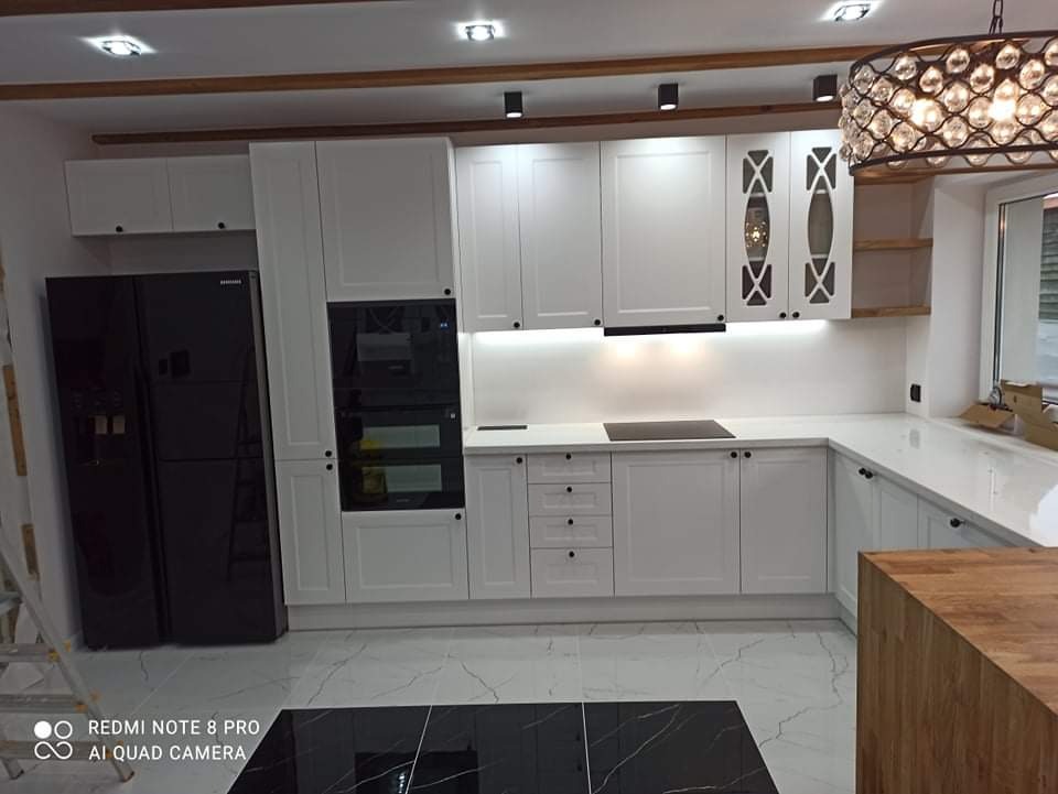 Nowoczesna kuchnia w bieli z czarnymi akcentami: zabudowa meblowa z frezowanymi frontami, czarny sprzęt AGD i marmurowa posadzka