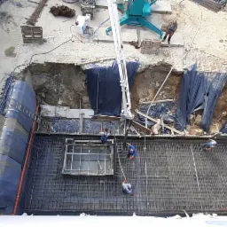 Budowa fundamentów w Konstancin-Jeziorna: widok z góry na wykop z ułożonym zbrojeniem i szalunkiem, pracownicy przy pracy, betonowóz w tle.