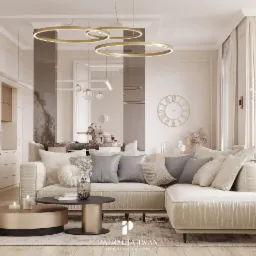 Jasny salon z narożną sofą z weluru, okrągłymi stolikami kawowymi w kolorze złota i czerni, oraz dekoracyjnymi lampami wiszącymi w kształcie złotych okręgów, widok na aneks kuchenny z przeszkloną...