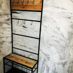 Metalowy wieszak z siedziskiem z drewnianymi elementami na tle ściany imitującej marmur.