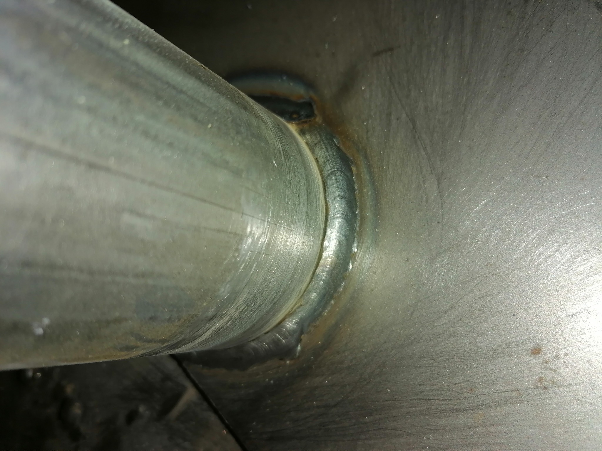 Szczegółowe zbliżenie na spoinę łączącą rurę z metalową powierzchnią, widoczne ślady obróbki i niedoskonałości spoiny.