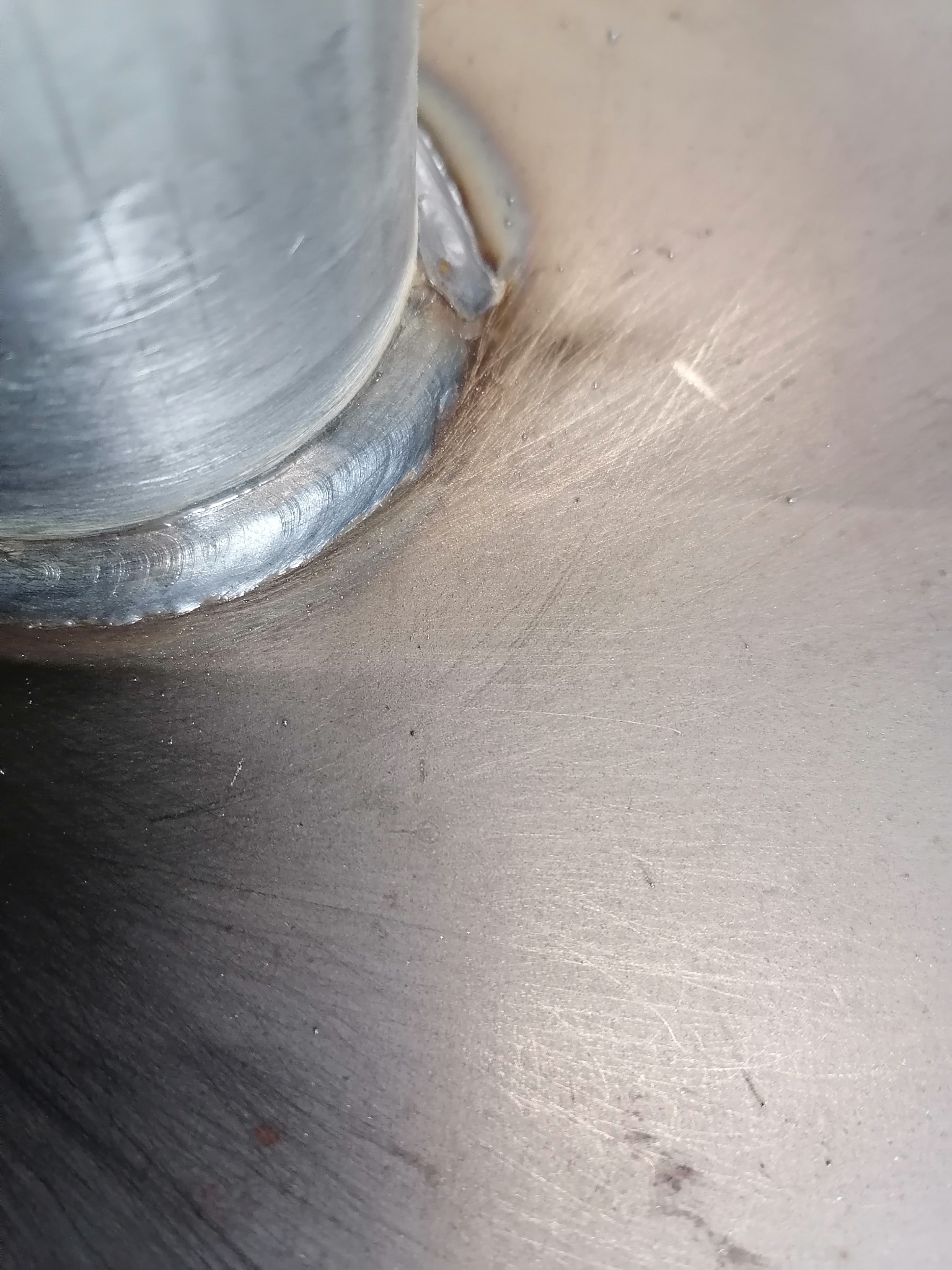 Szczegółowe ujęcie spoiny łączącej rurę ze stalową powierzchnią, widoczne ślady szlifowania i obróbki metalu.