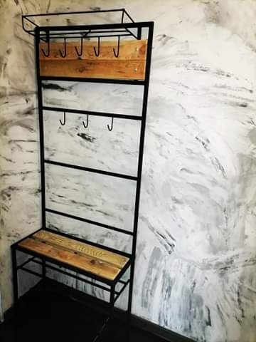 Metalowy wieszak z siedziskiem z drewnianymi elementami na tle ściany imitującej marmur.