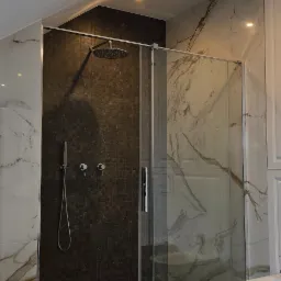 Nowoczesna łazienka z kabiną prysznicową typu walk-in, wykończona płytkami imitującymi marmur i mozaiką, oświetlona punktowymi lampami sufitowymi.