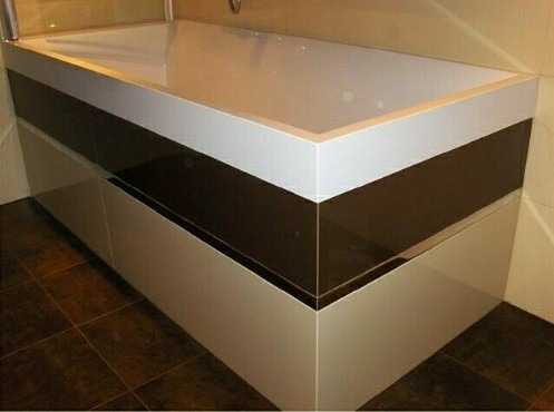 Nowoczesna obudowa wanny z białym blatem i ciemnobrązowym pasem, wykończona płytkami podłogowymi w odcieniach brązu.